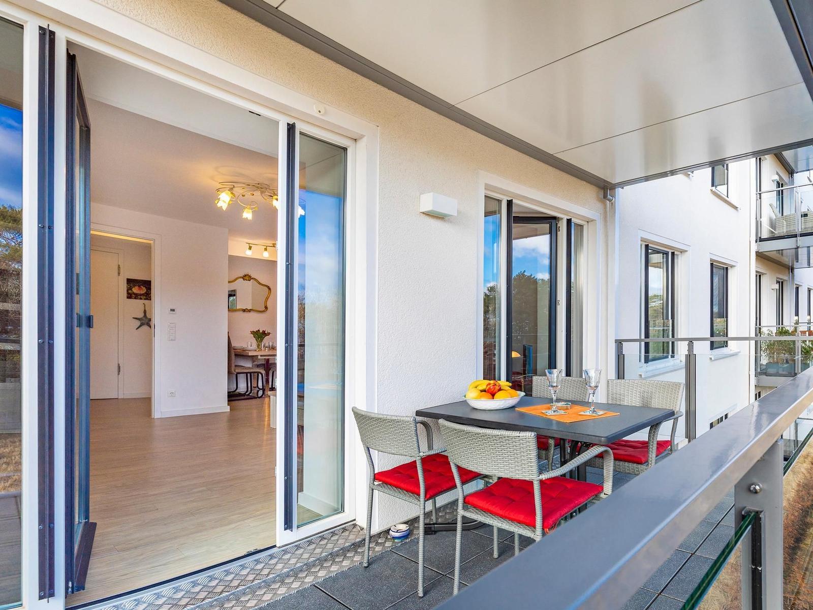 Terrasse mit Tisch, Stühlen und Obst. Durchgehende Glasschiebetüren führen ins Innere.