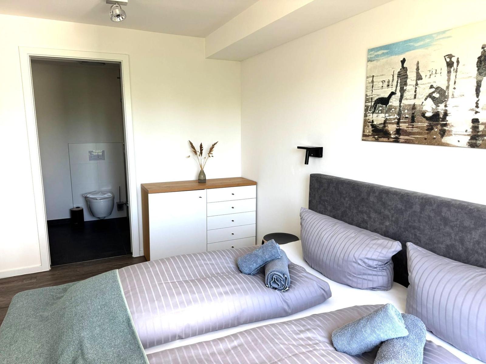 Schlafzimmer mit Doppelbett, Schrank und Bad im Anschluss.