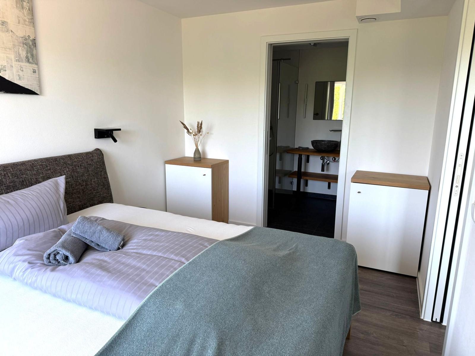 Schlafzimmer mit Bett, Kleiderschrank und angrenzender Dusche.