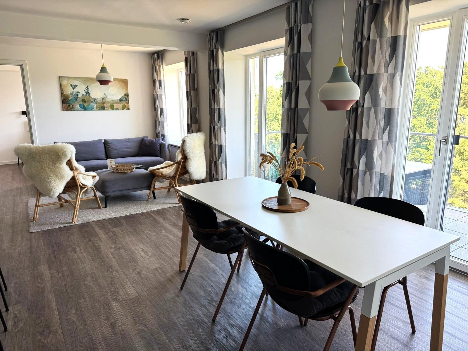Essbereich mit Tisch und Stühlen. Wohnbereich mit Sofa und Sitzgelegenheiten. Balkon mit Blick auf Grün.