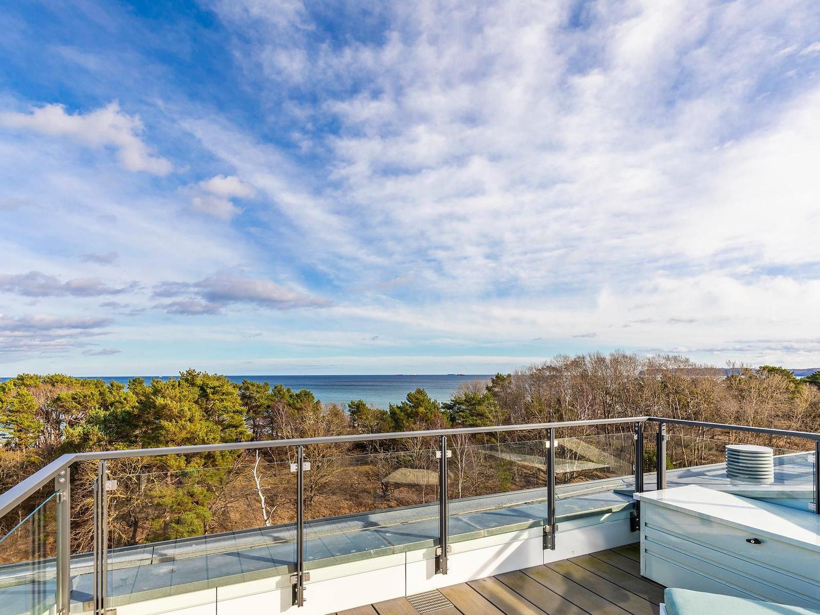 Terrasse mit Glasgeländer und Blick auf Meer und Wald.