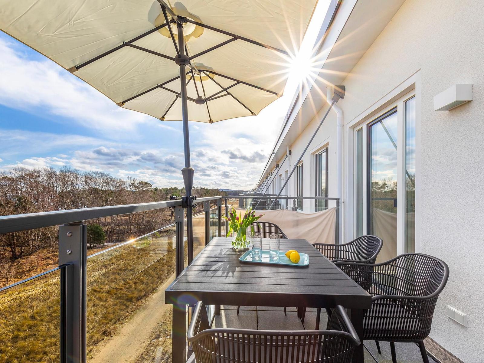 Terrasse mit Tisch, Stühlen und Sonnenschutz. Blick auf Wald und Himmel.