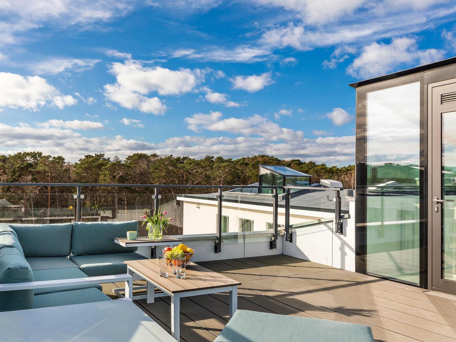 Terrasse mit Sitzgruppe, Tisch und Blick auf Wald und Himmel.