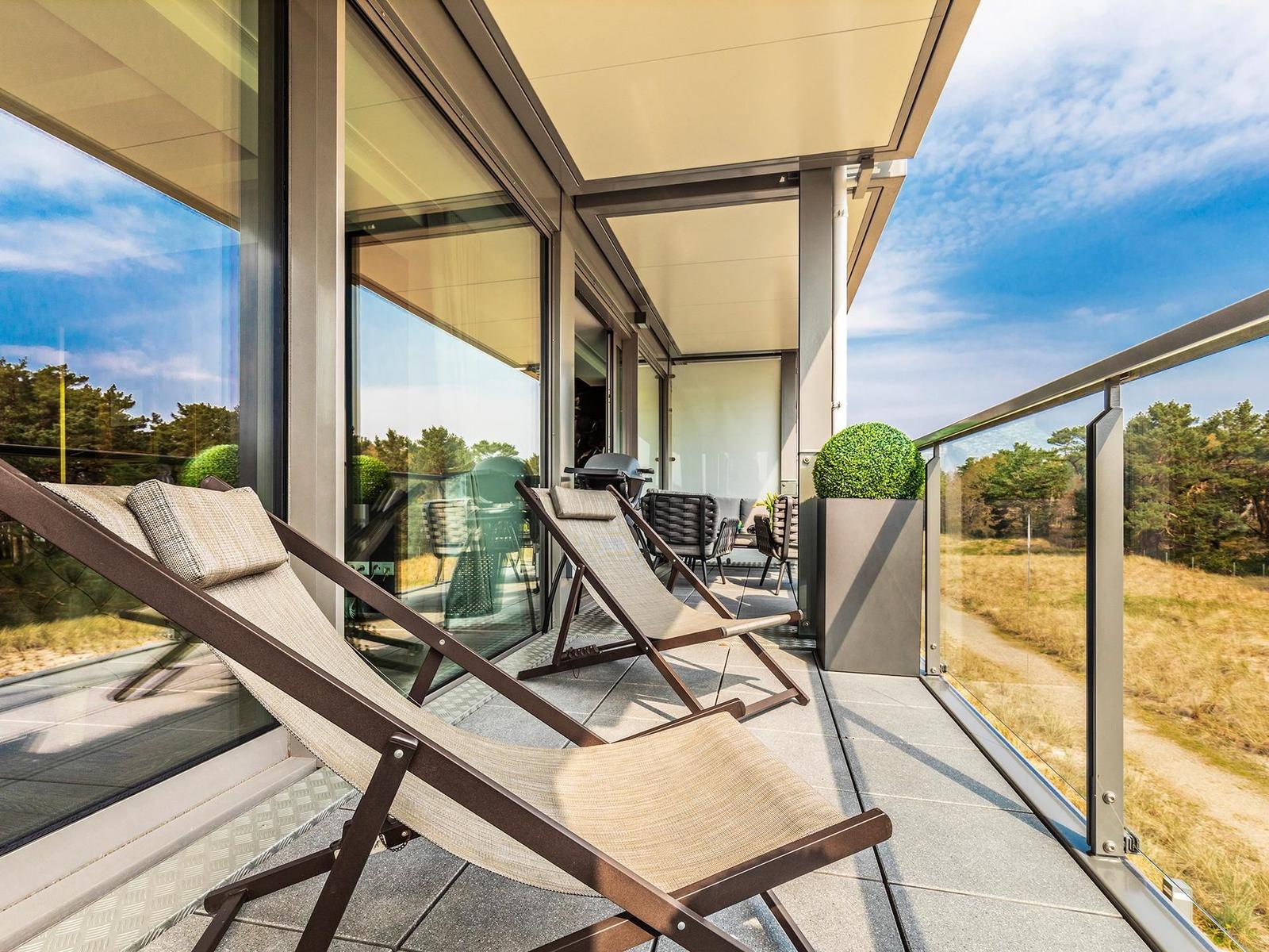 Terrasse mit Liegestühlen und Blick auf Wald. Glasgeländer und Pavillon sichtbar.