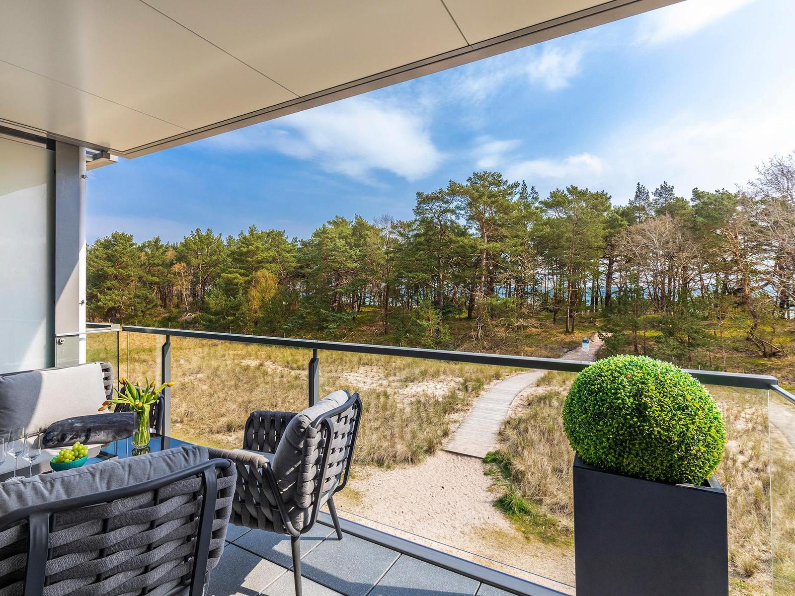 Terrasse mit Sitzgelegenheiten und Blick auf Wald und Strandweg.