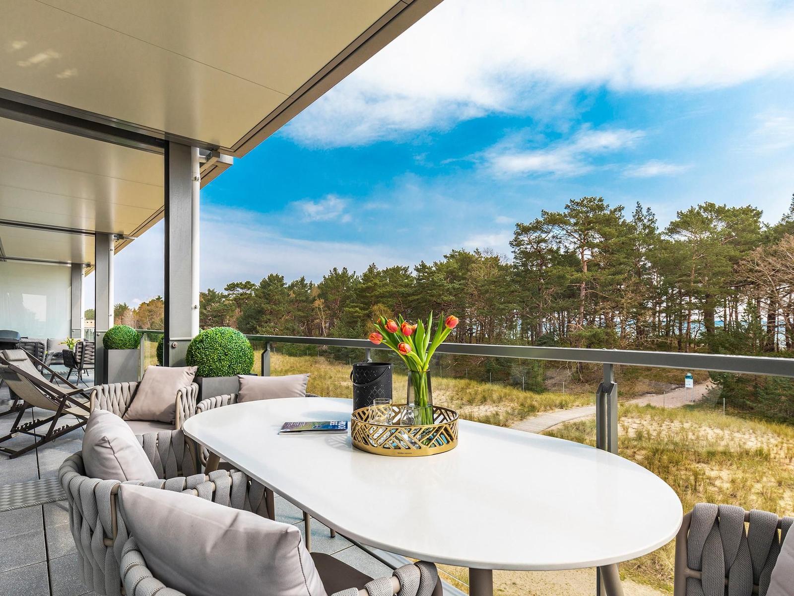 Terrasse mit Tisch, Stühlen und Blick auf Wald und Himmel.