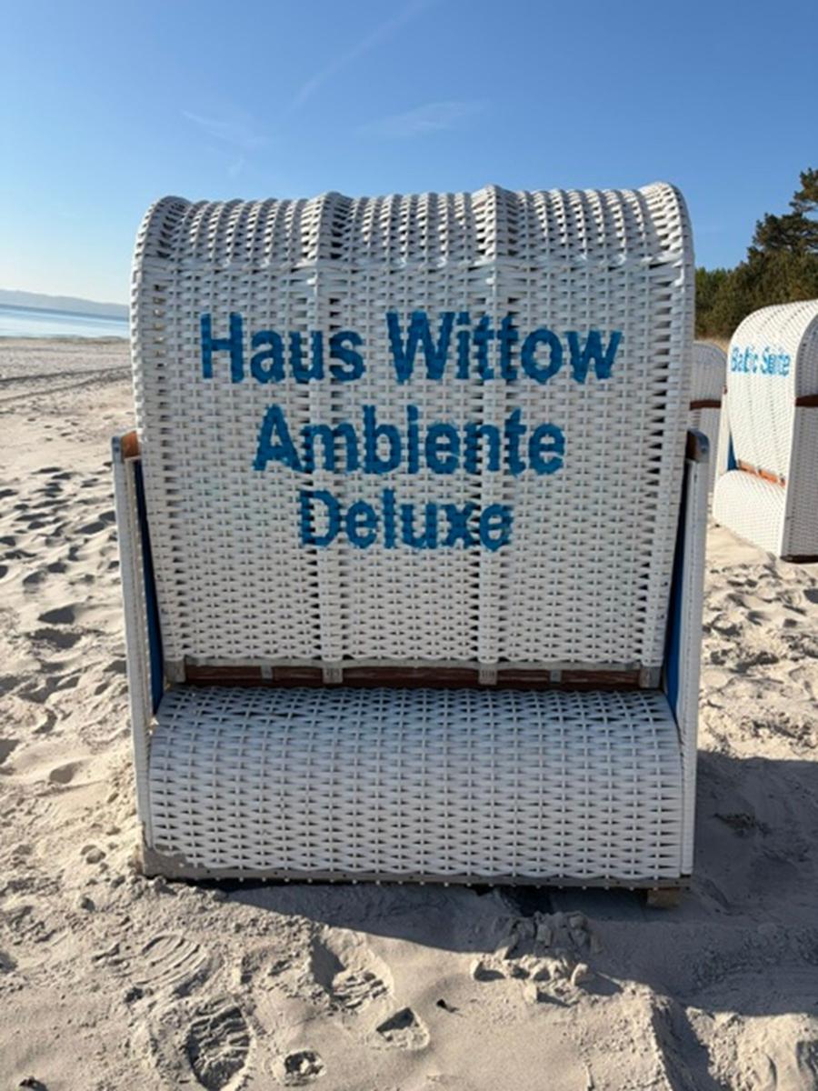 Weißer Strandkorb mit Aufschrift Haus Wittow Ambiente Deluxe steht am Strand.