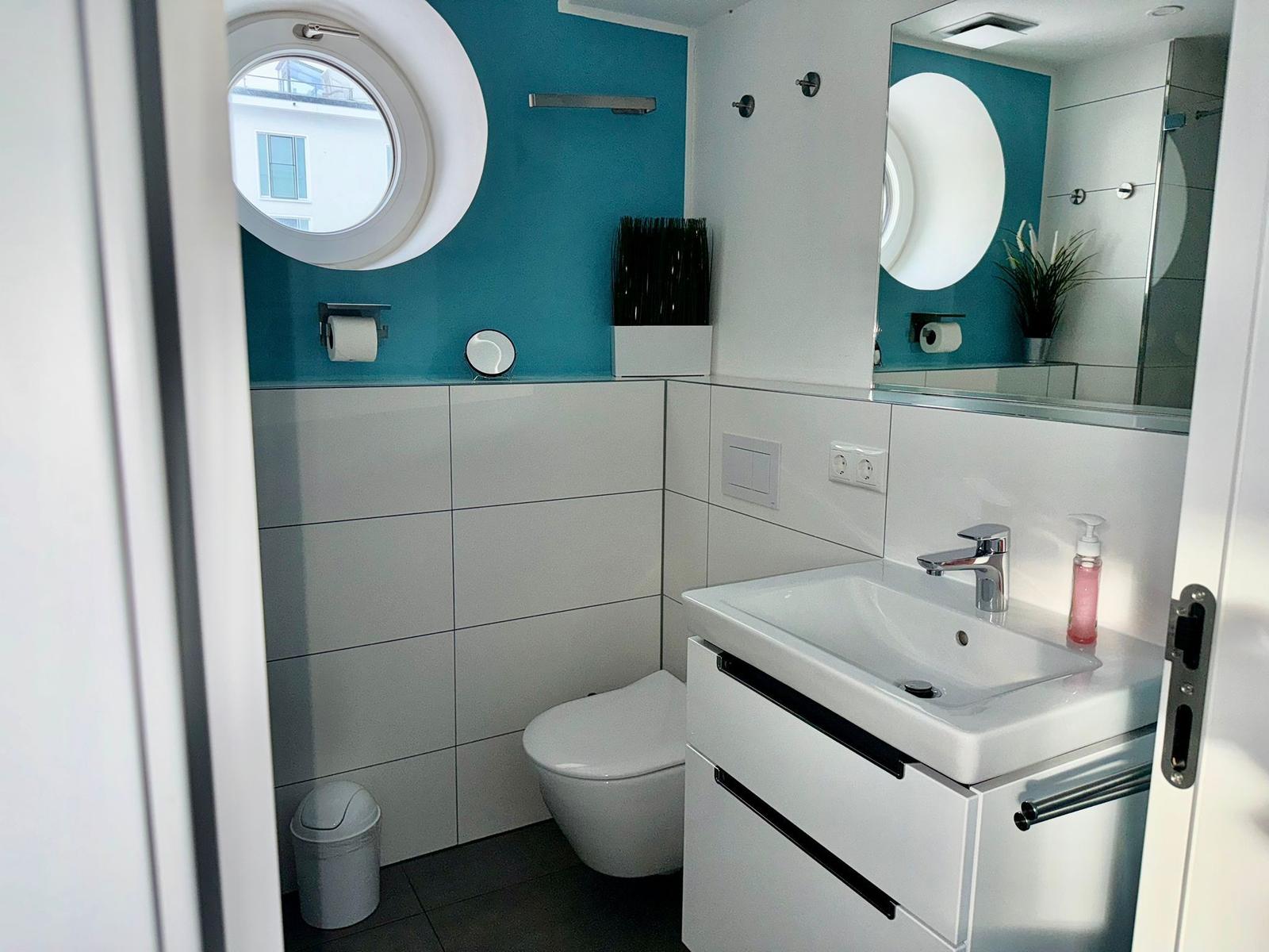 Badezimmer mit Toilette, Waschbecken und runden Fenster. Wandfarbe türkis.