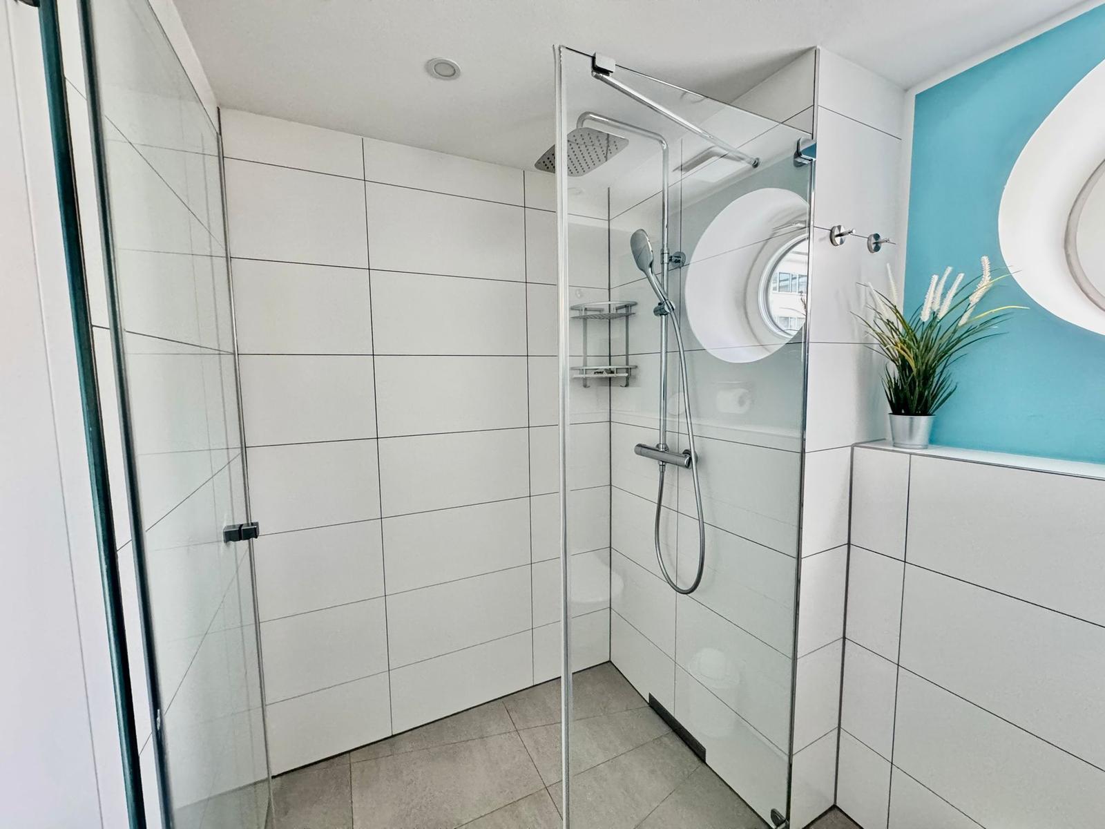 Dusche mit Glaswand, Duschbrause und runden Fenster