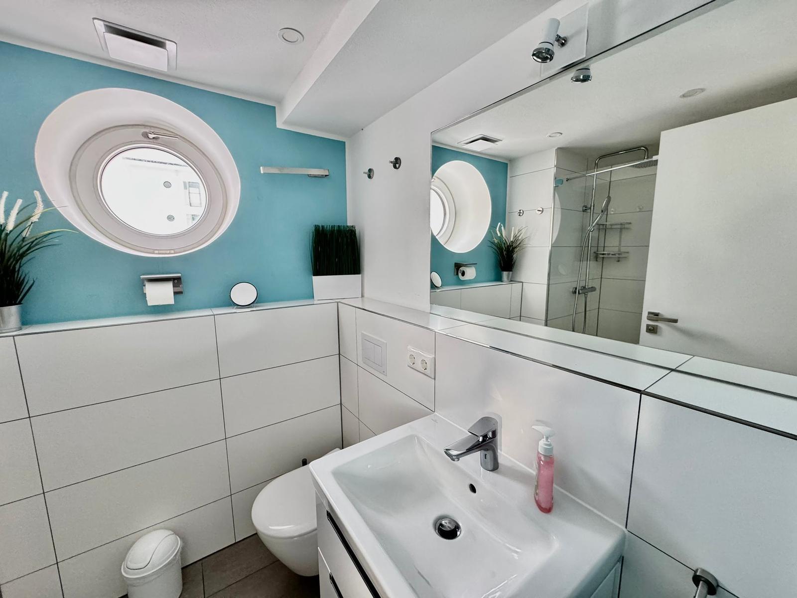 Badezimmer mit runden Fenster, Waschbecken und Dusche.