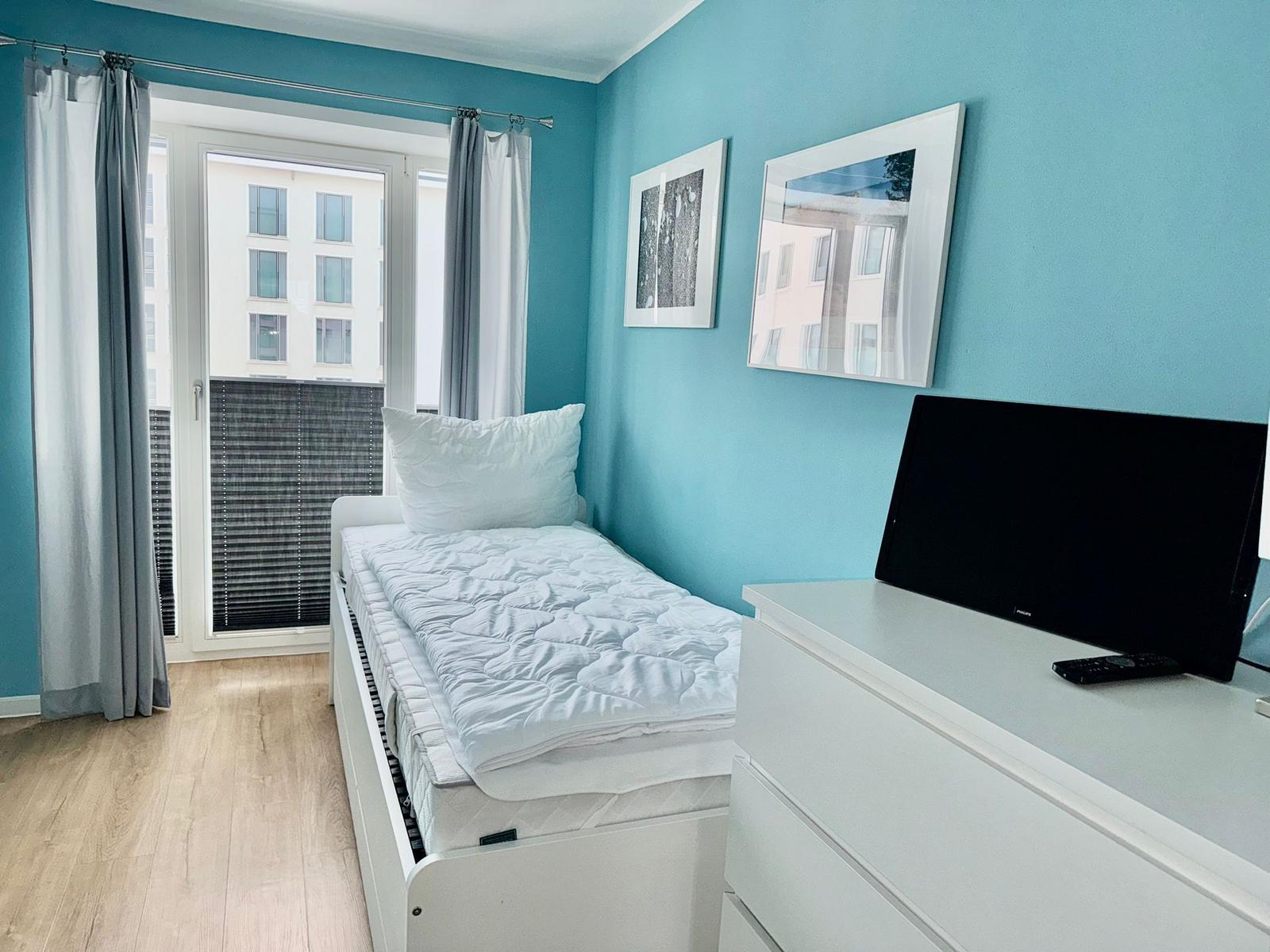 Schlafzimmer mit Bett, Fernseher und Fenster zum Balkon.