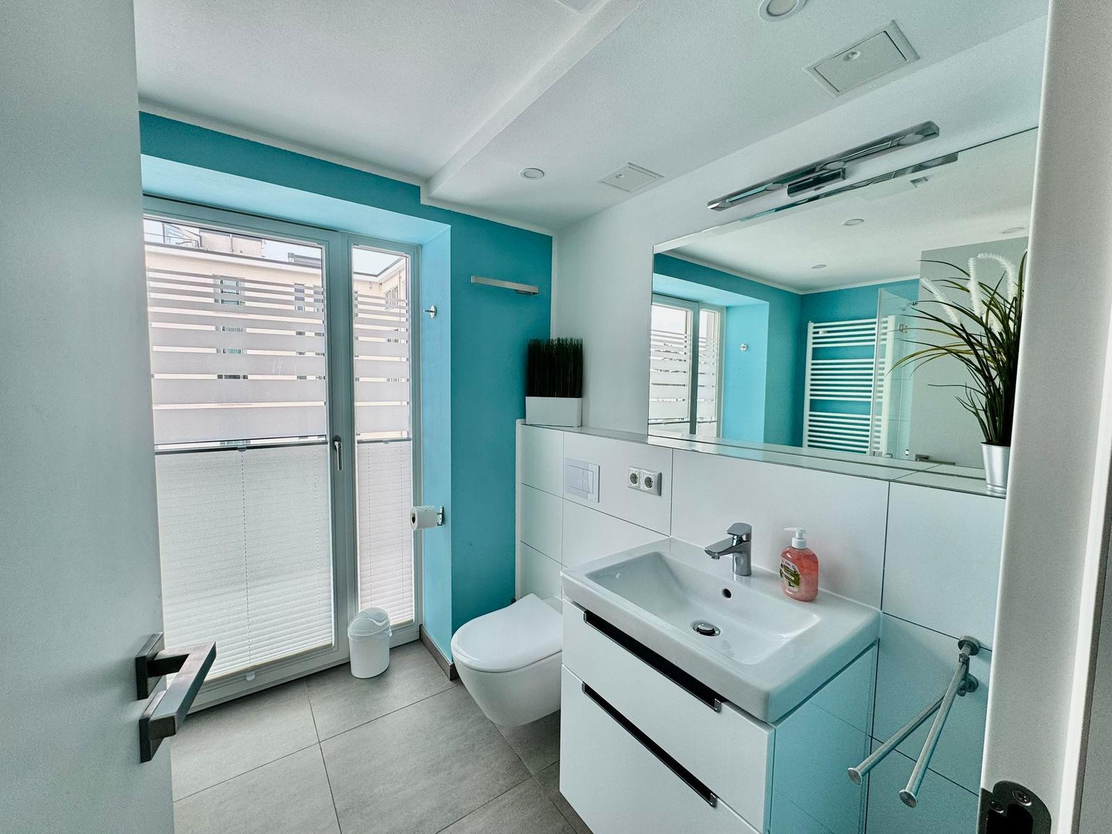 Badezimmer mit Waschbecken, Toilette und Glastür zum Balkon.