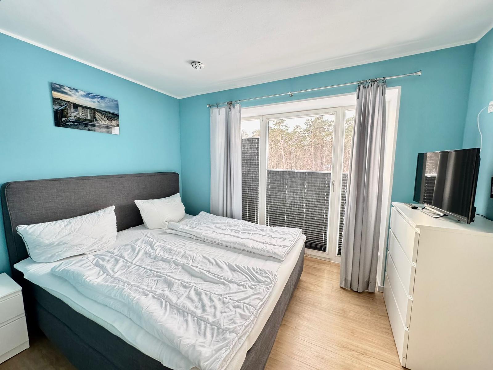 Schlafzimmer mit Bett, TV und Balkonansicht.