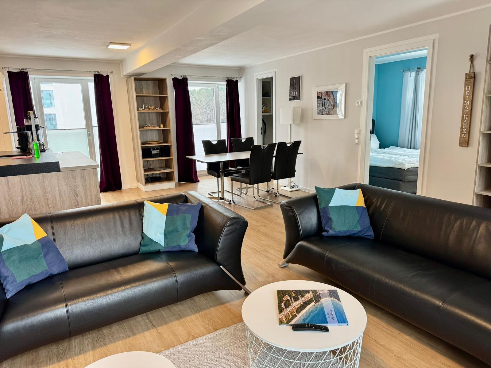 Wohnbereich mit zwei Ledersofas, Esstisch und Blick in Schlafzimmer.