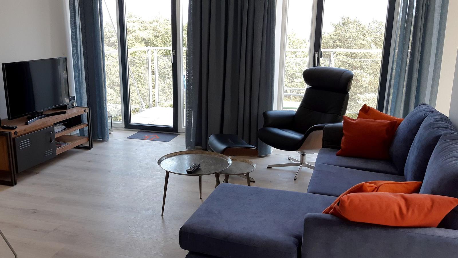 Wohnzimmer mit Sofa, Sessel, TV und Balkonblick.