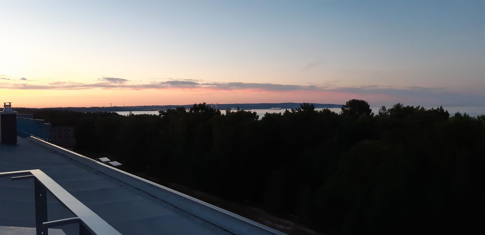Terrasse mit Blick auf Wald und Wasser bei Sonnenuntergang.