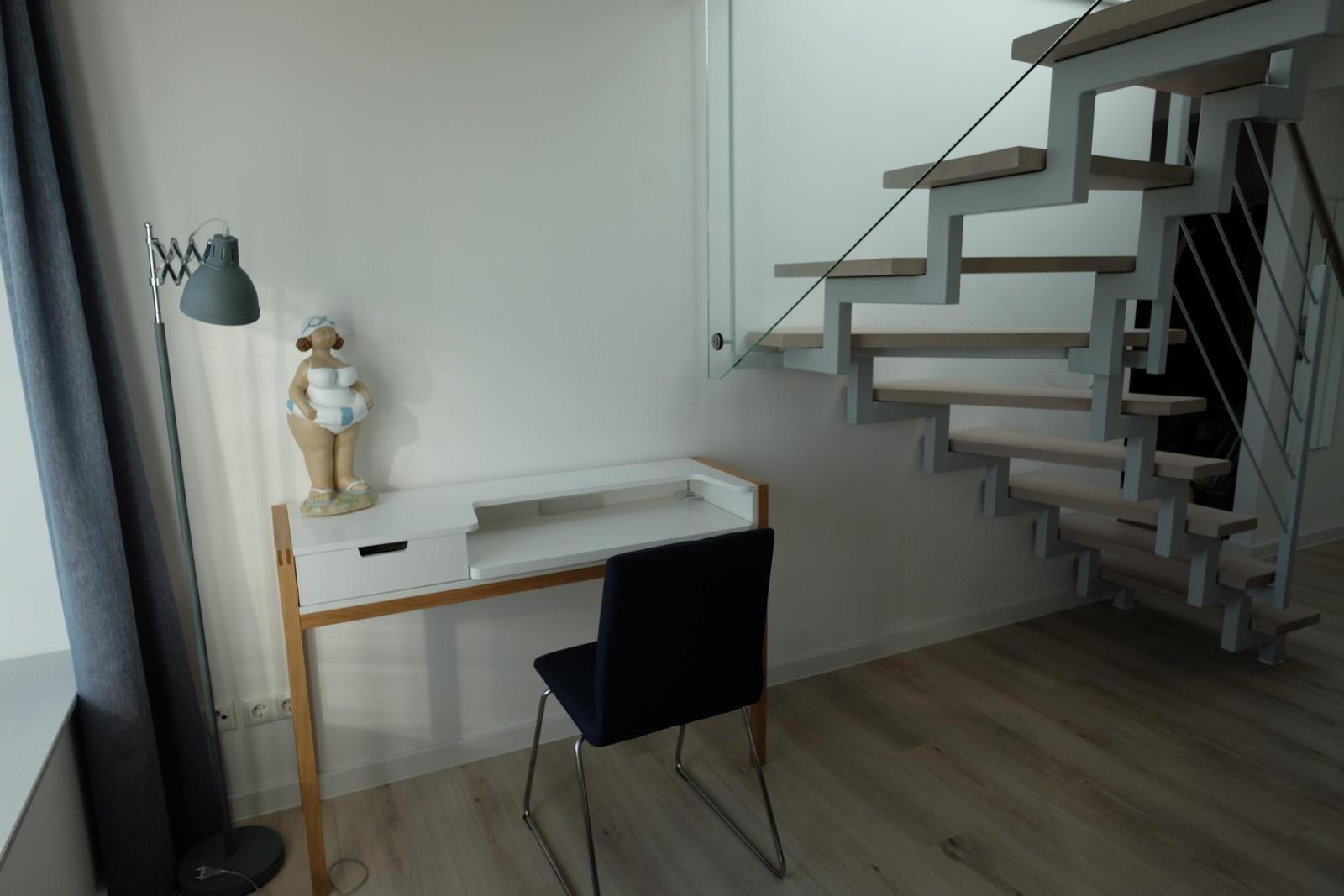 Schreibtisch mit Stuhl und Lampe neben einer Treppe.