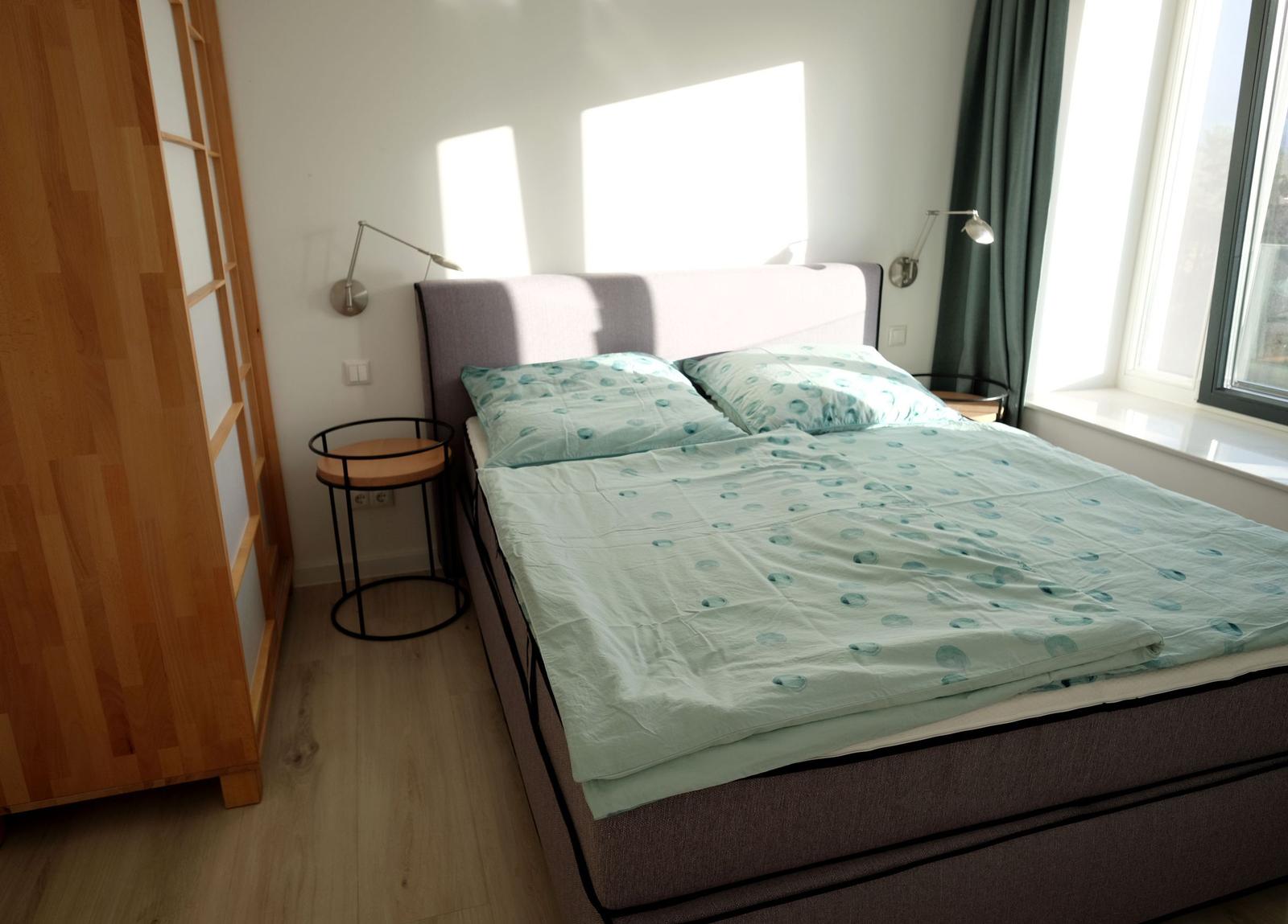 Schlafzimmer mit Bett, Nachttisch und Fenster.
