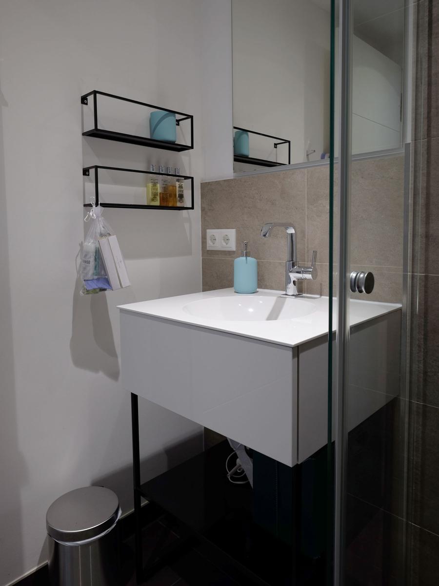 Waschbecken mit Spiegelschrank, Duschbereich und Aufbewahrungsmöbel.