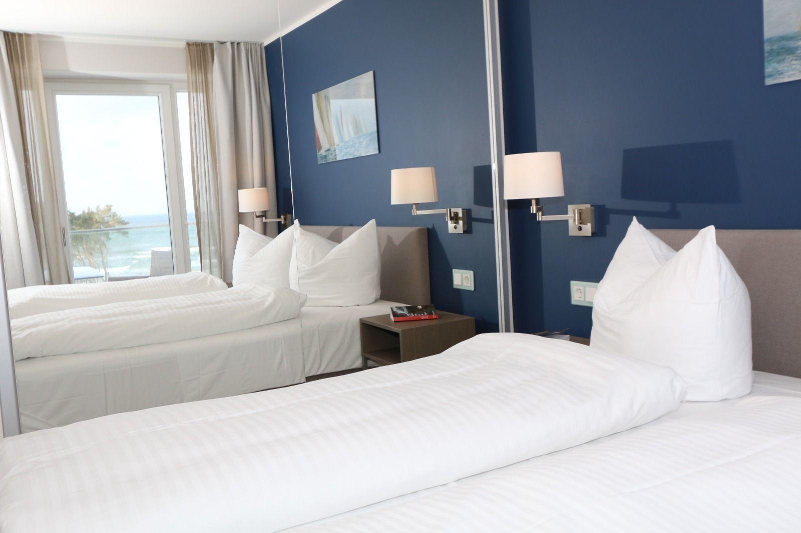 Zimmer mit zwei Betten, blauer Wand und Meerblick durch Fenster.