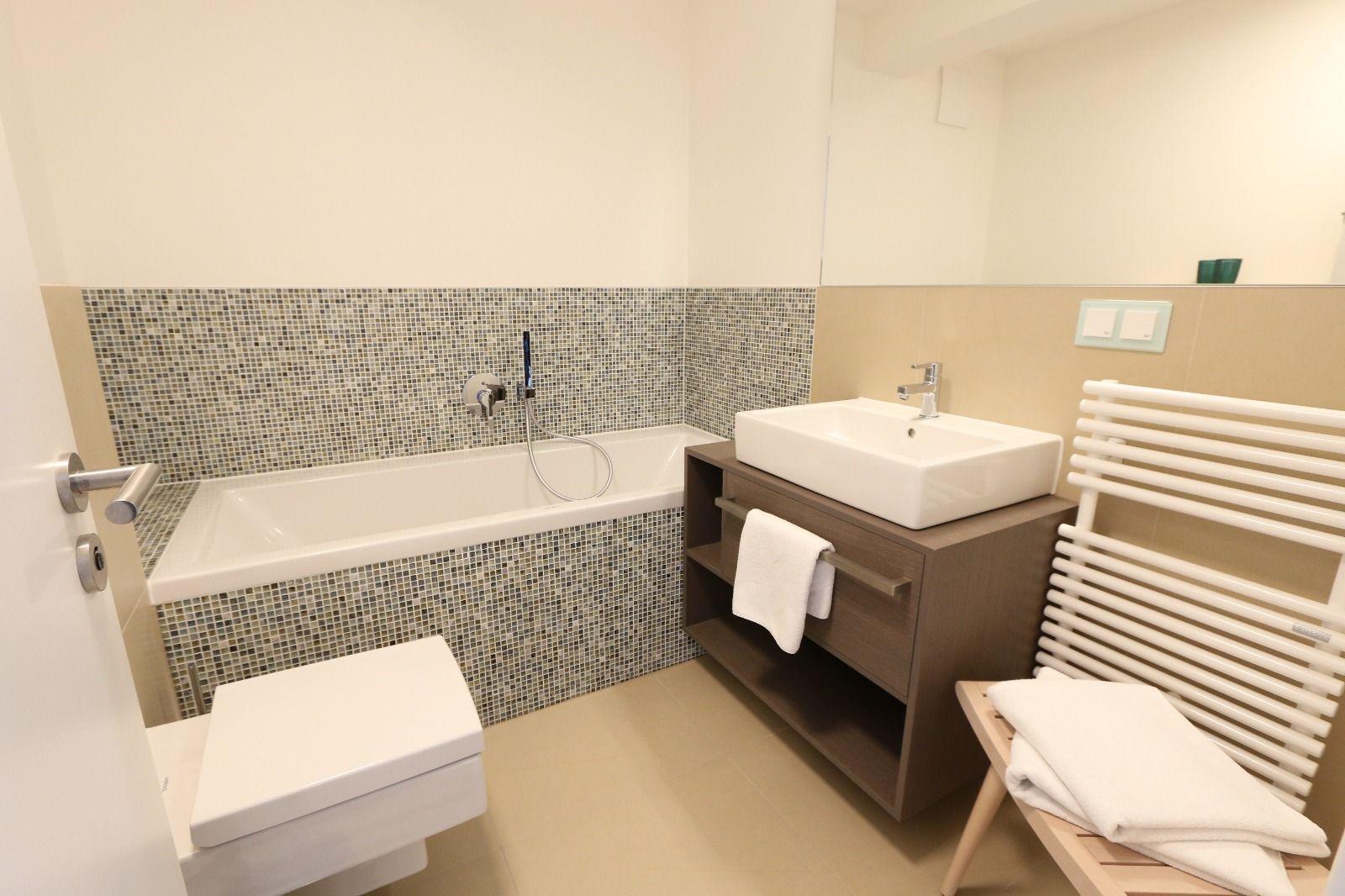 Badezimmer mit Badewanne, Waschbecken und Toilette. Mosaikfliesen an der Wand.
