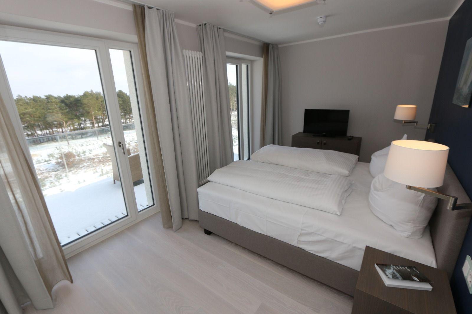 Schlafzimmer mit Doppelbett, Fernseher und Balkon mit Blick auf Wald.