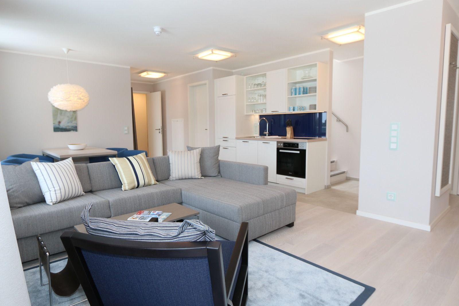 Wohnbereich mit Sofa, Küchenzeile und Tisch. Helle Farben und modernes Design.