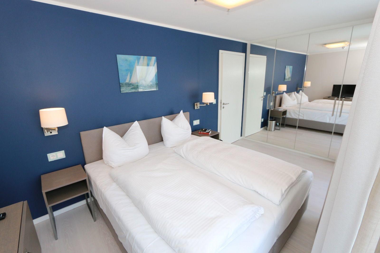 Schlafzimmer mit Doppelbett, blauer Wand und Spiegelschrank.