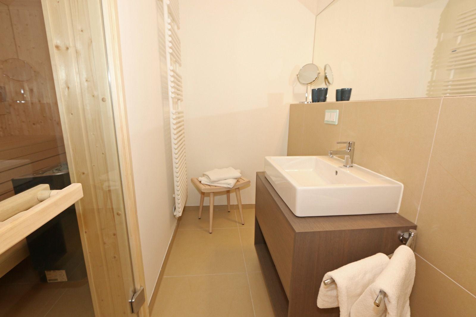Badezimmer mit Waschbecken, Spiegel und Sauna. Holzstuhl und Handtücher.