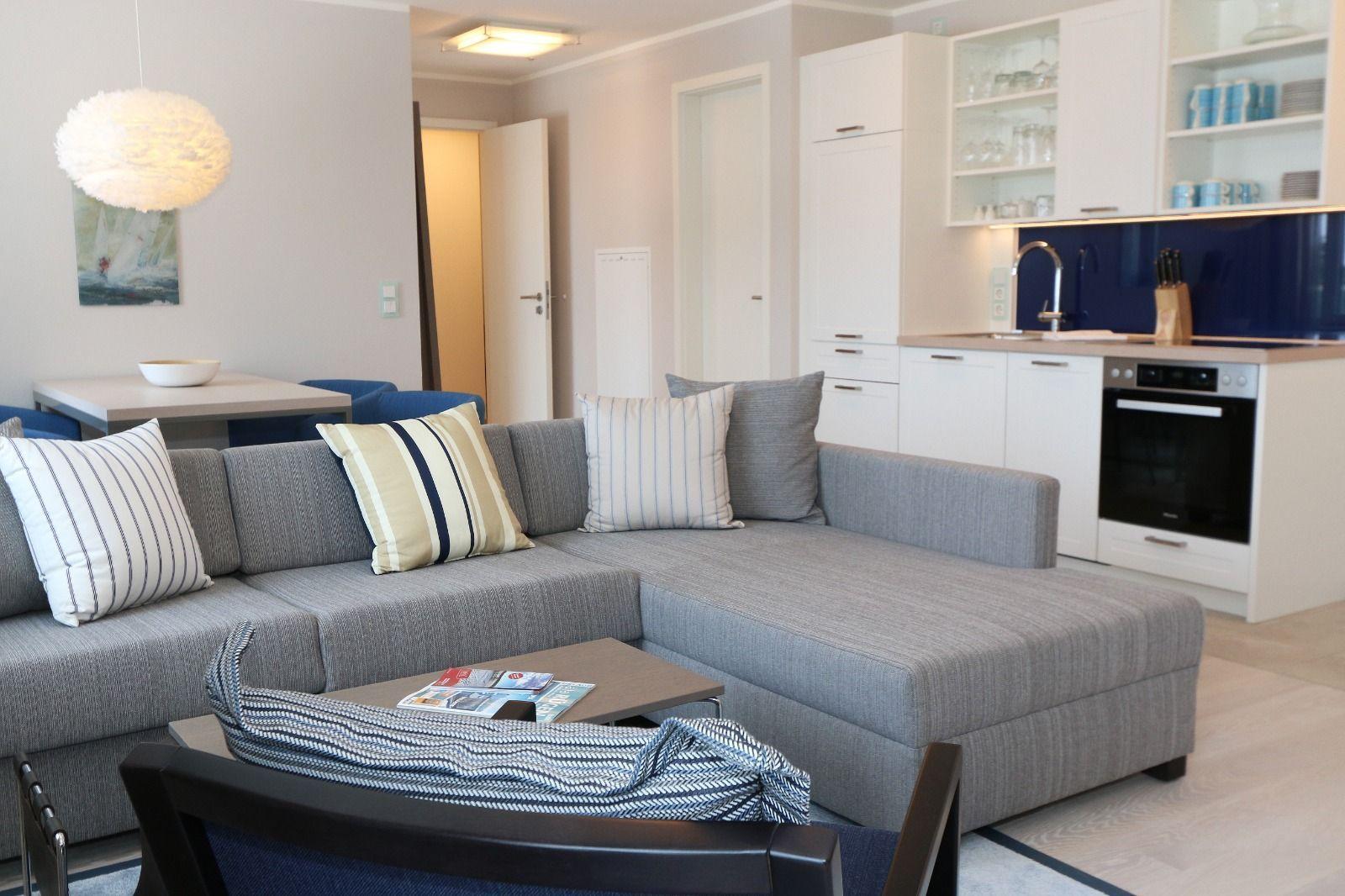 Wohnbereich mit Sofa, Couchtisch und Küchenzeile mit weißen Schränken.