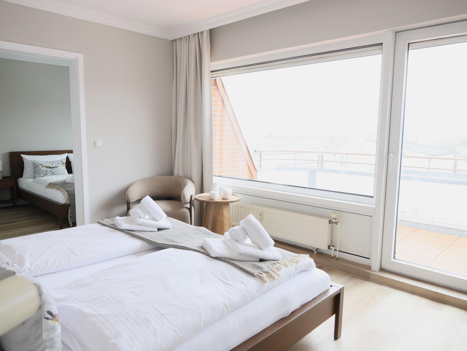 Schlafzimmer mit Doppelbett, Sitzgelegenheit und Blick auf Balkon.