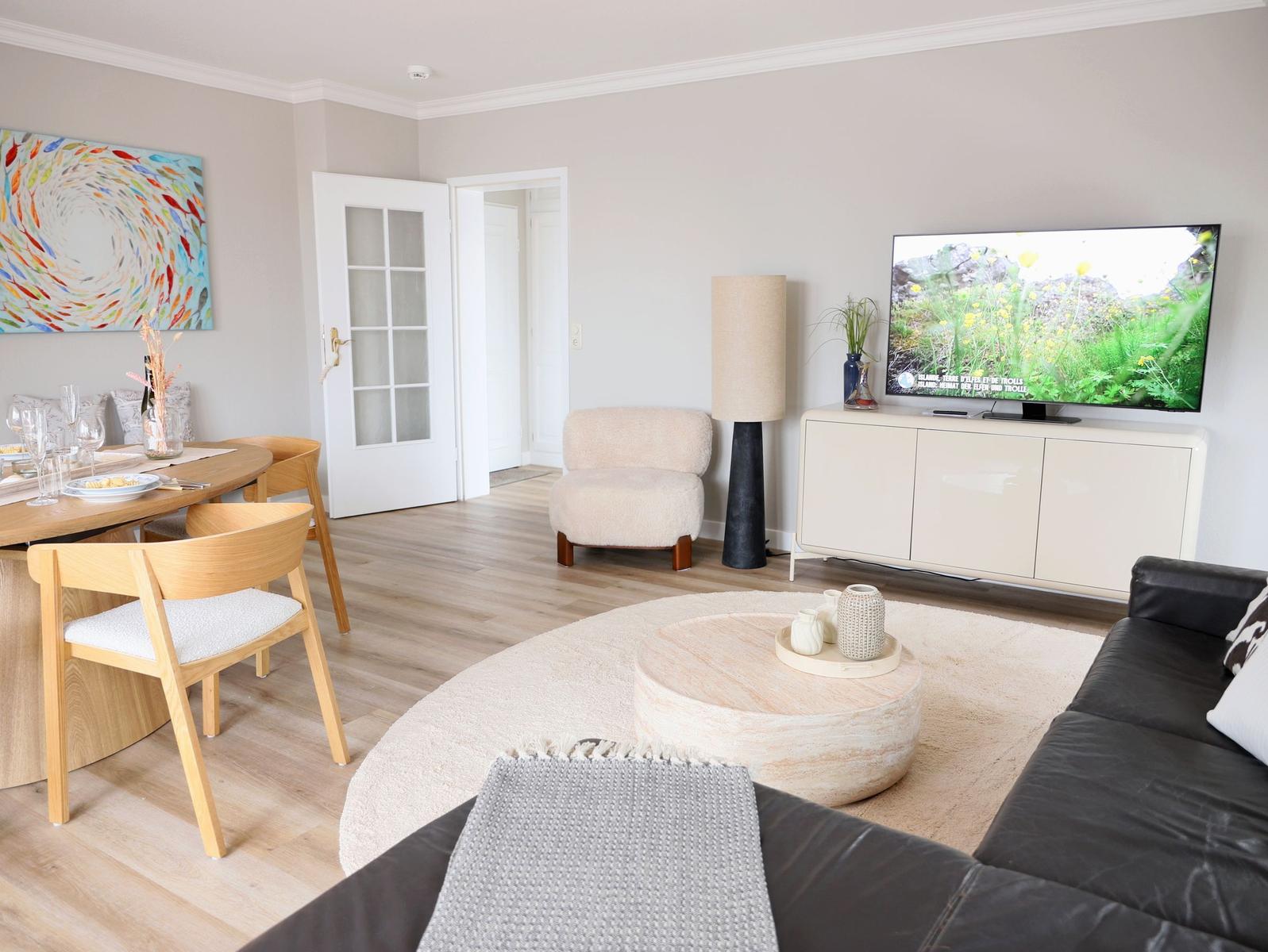 Wohn- und Essbereich mit TV, Sofa, Esstisch und Kunstwerk an der Wand.