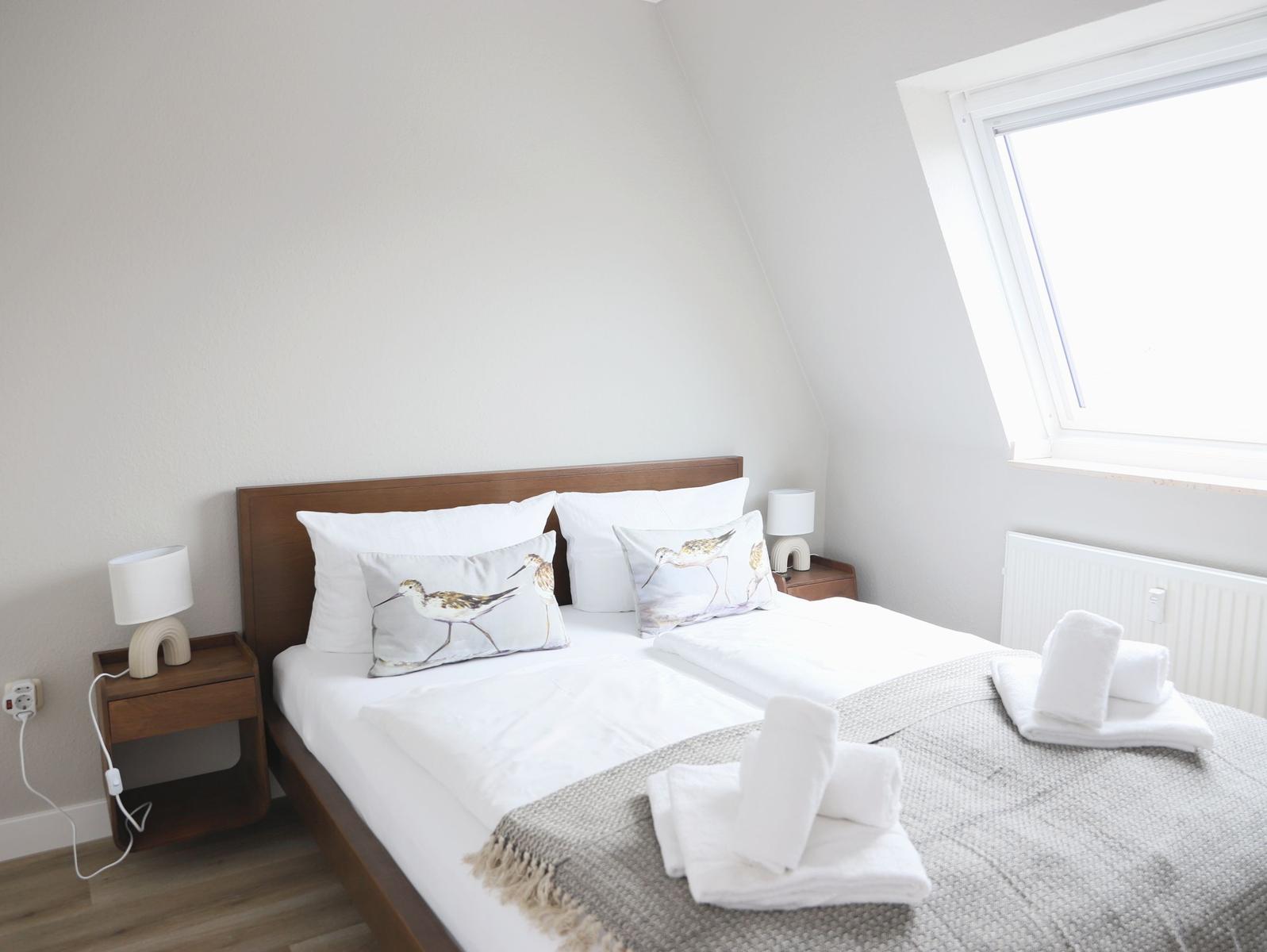 Schlafzimmer mit Dachschrägen, Bett mit Kissen, Nachttisch und Fenster.