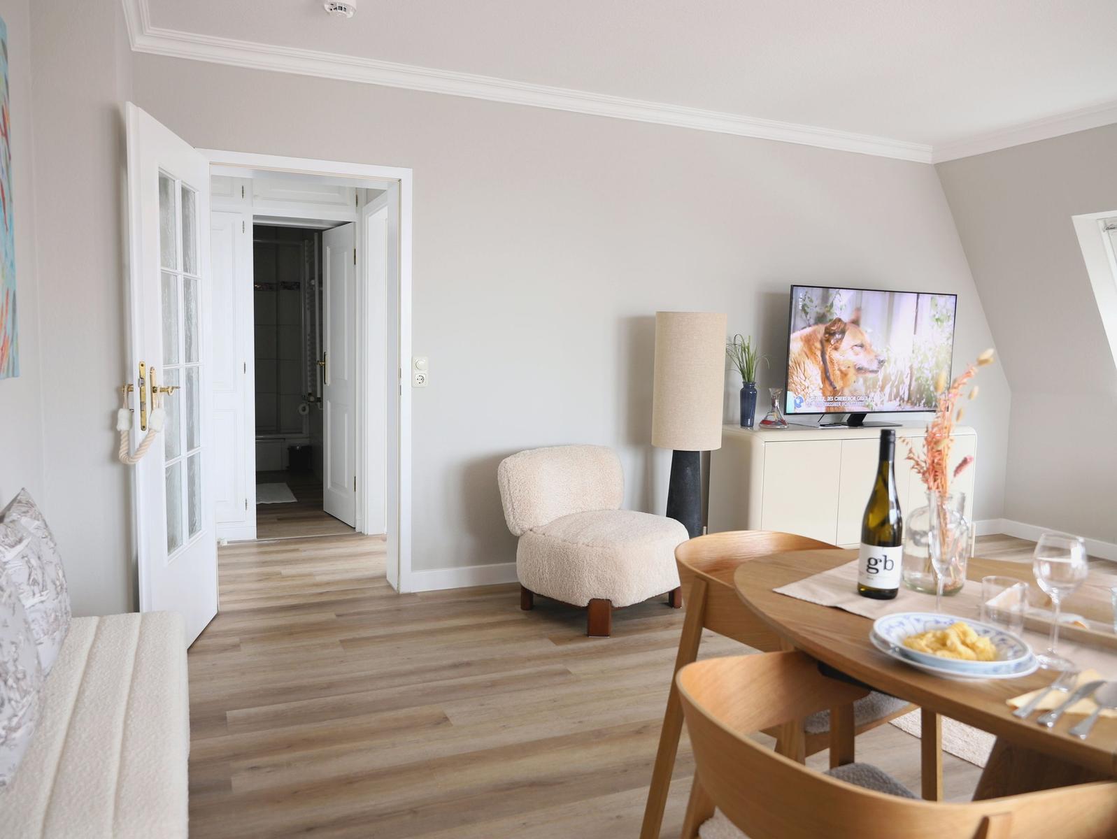 Wohnbereich mit Esstisch, Fernseher und Blick in das Badezimmer.