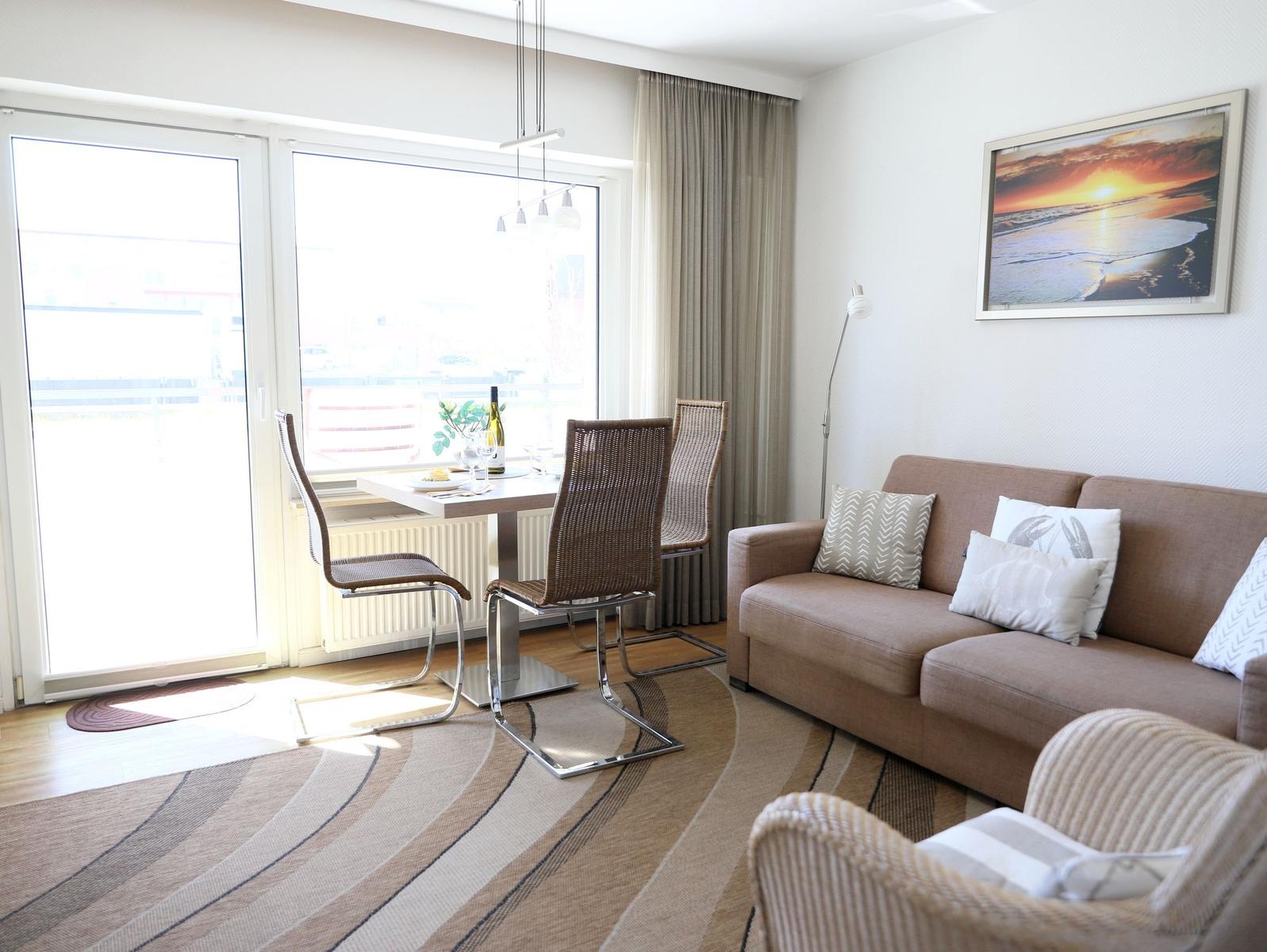 Living and dining area with sofa, table and chairs. Large windows and wall picture.