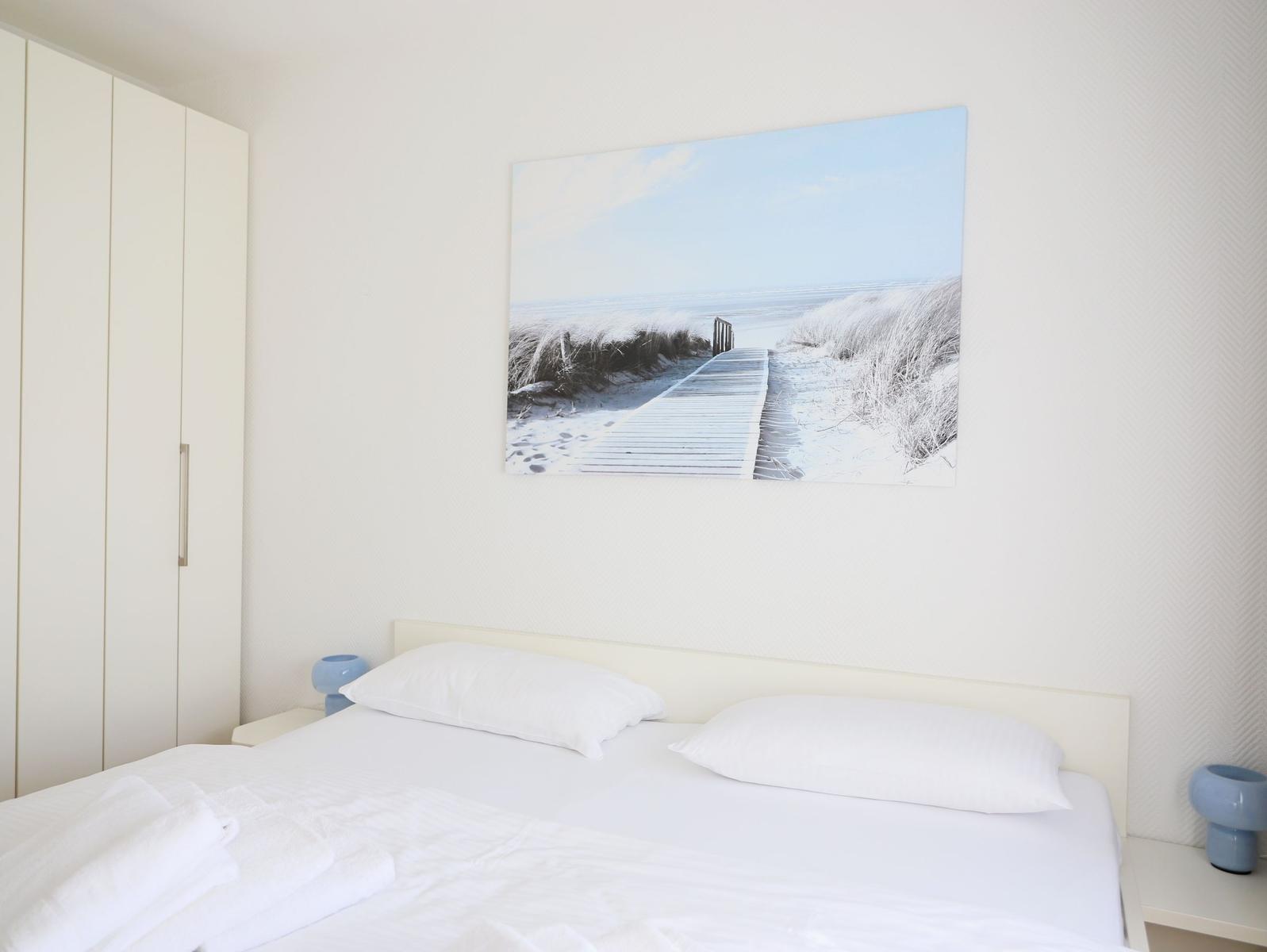 Bedroom with white bed, wall art, and wardrobe