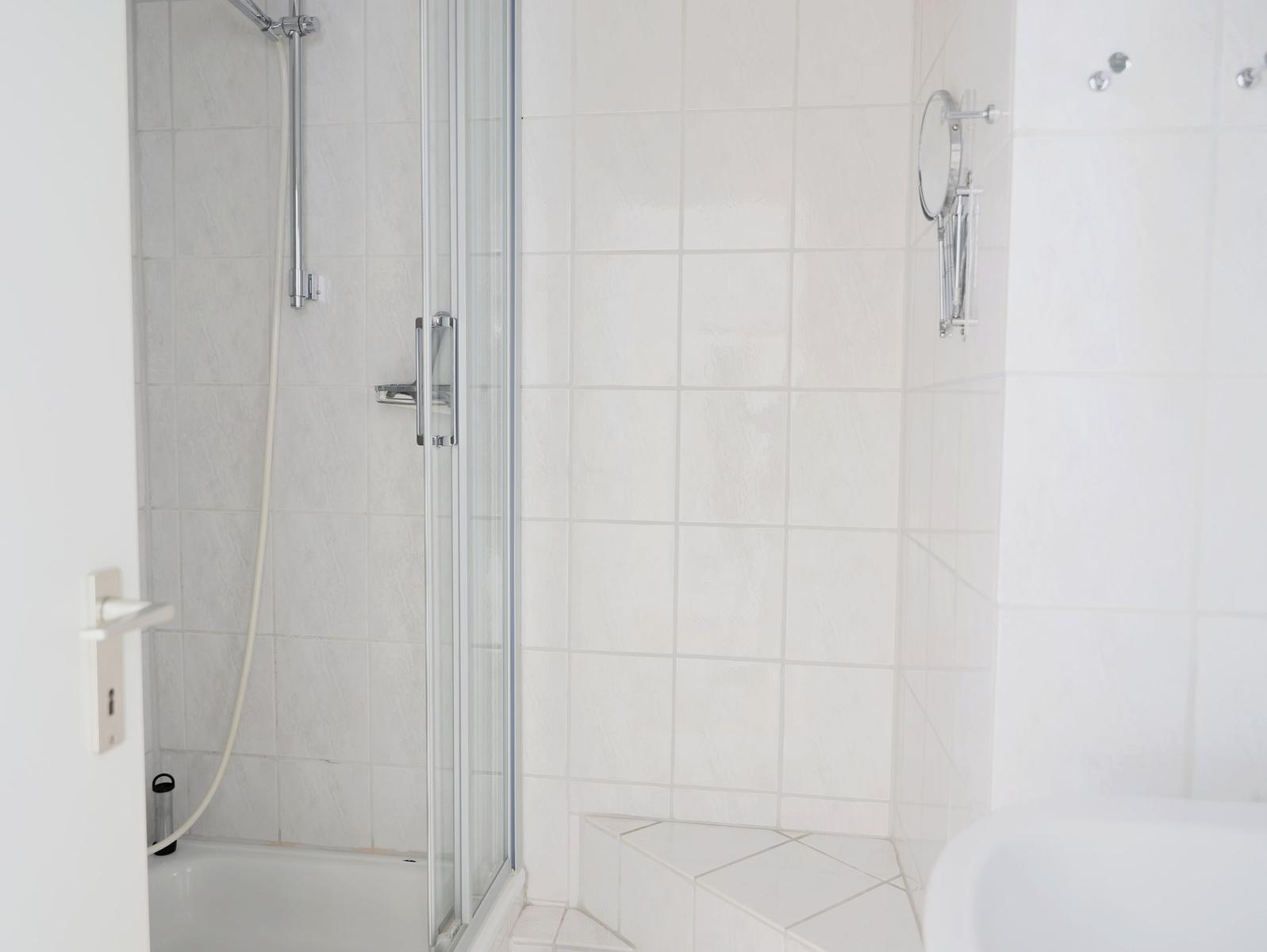 Shower with glass enclosure and shower head, white tiles and mirror