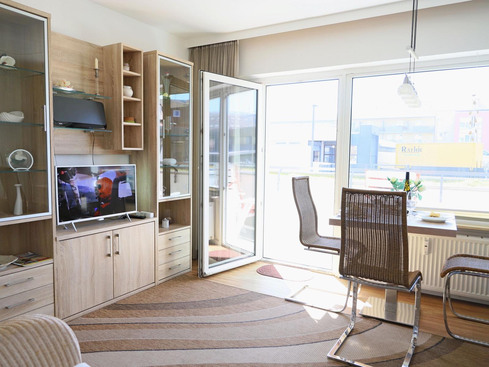 Living room with TV, dining area, and balcony door. Furniture and fittings are modern.