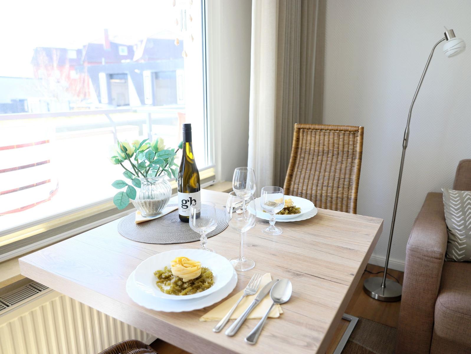 Dining table with two plates, wine bottle, and chairs by window with view.