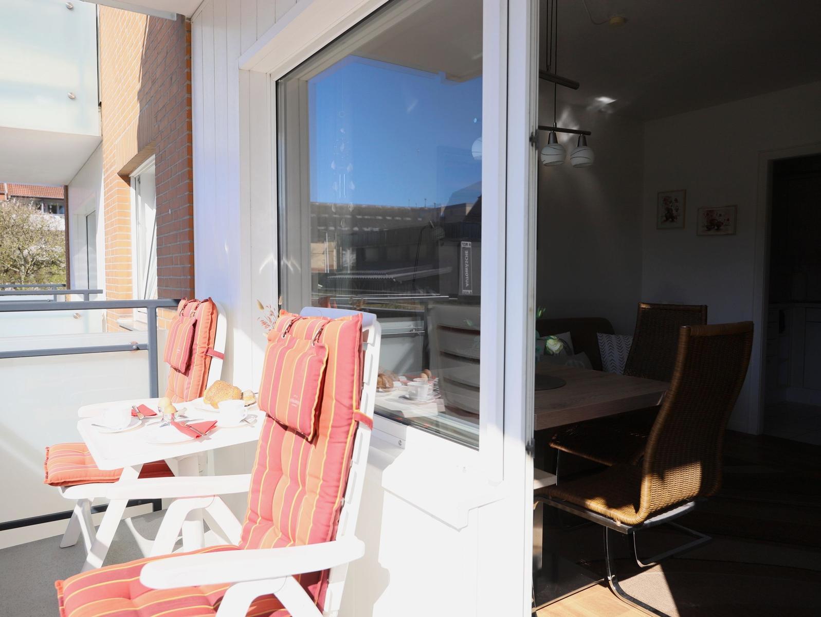 Terrace with table and chairs with orange cushions. Dining room visible through glass door.