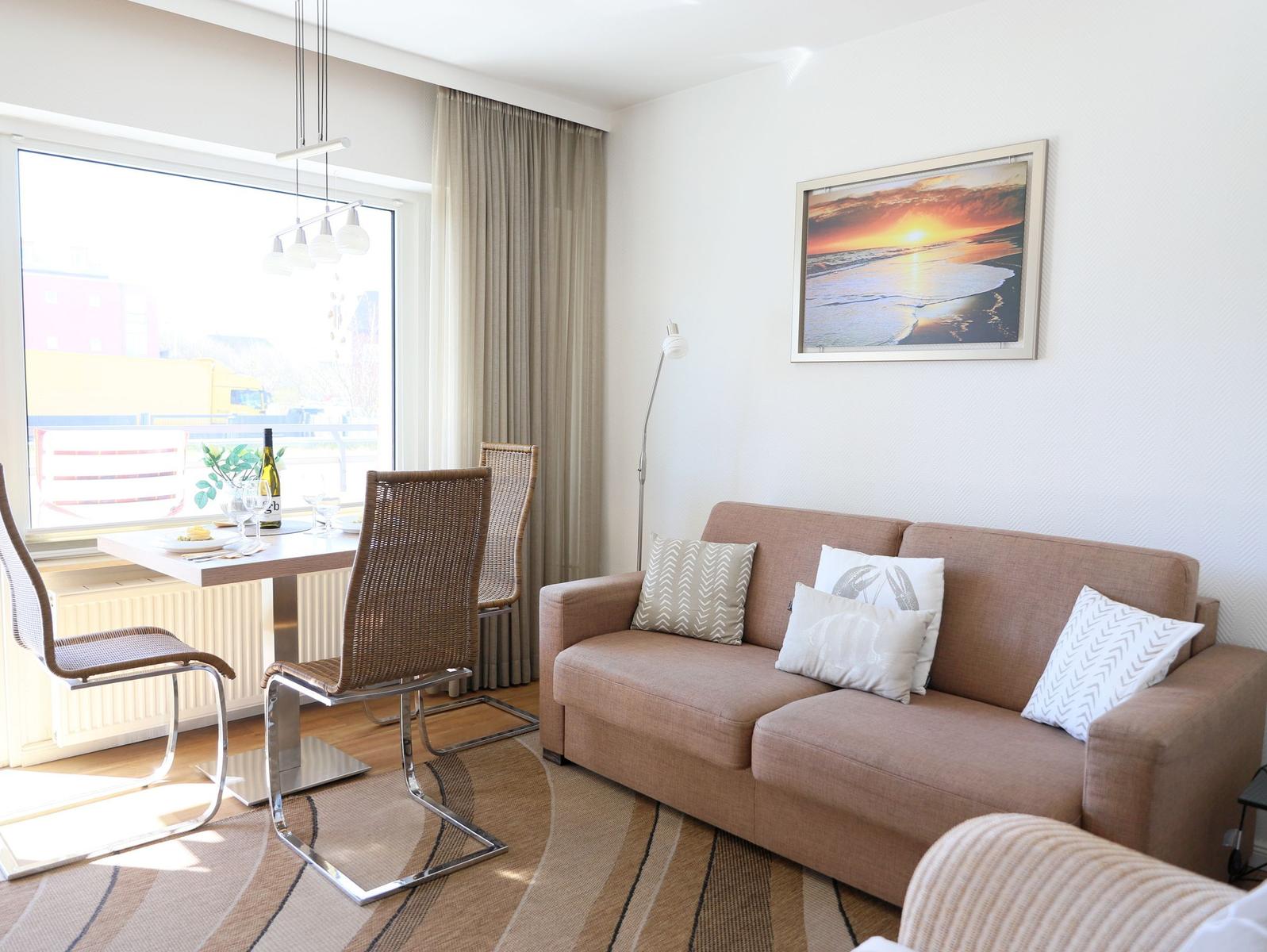 Living room with sofa, table and chairs, wall art and large window.