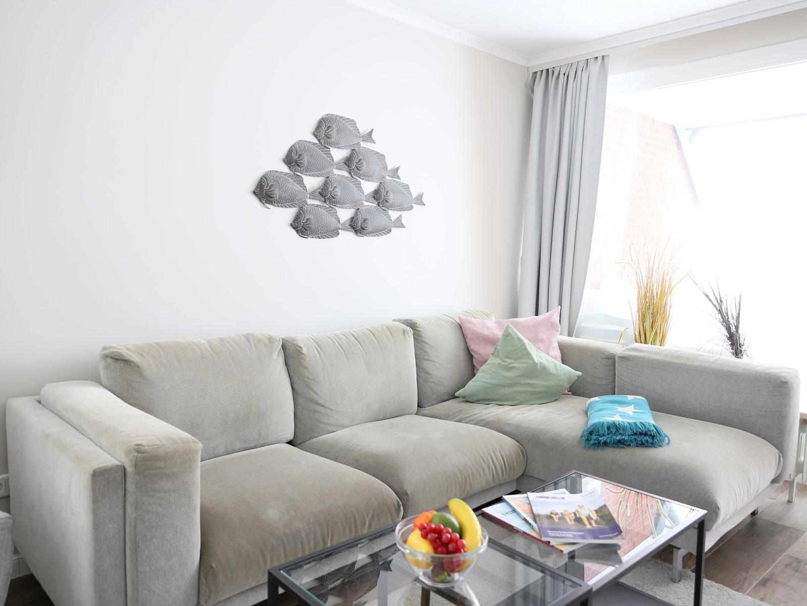 Ein Wohnzimmer mit grauem Sofa, dekorativen Kissen und einer Wanddekoration aus Fischen.