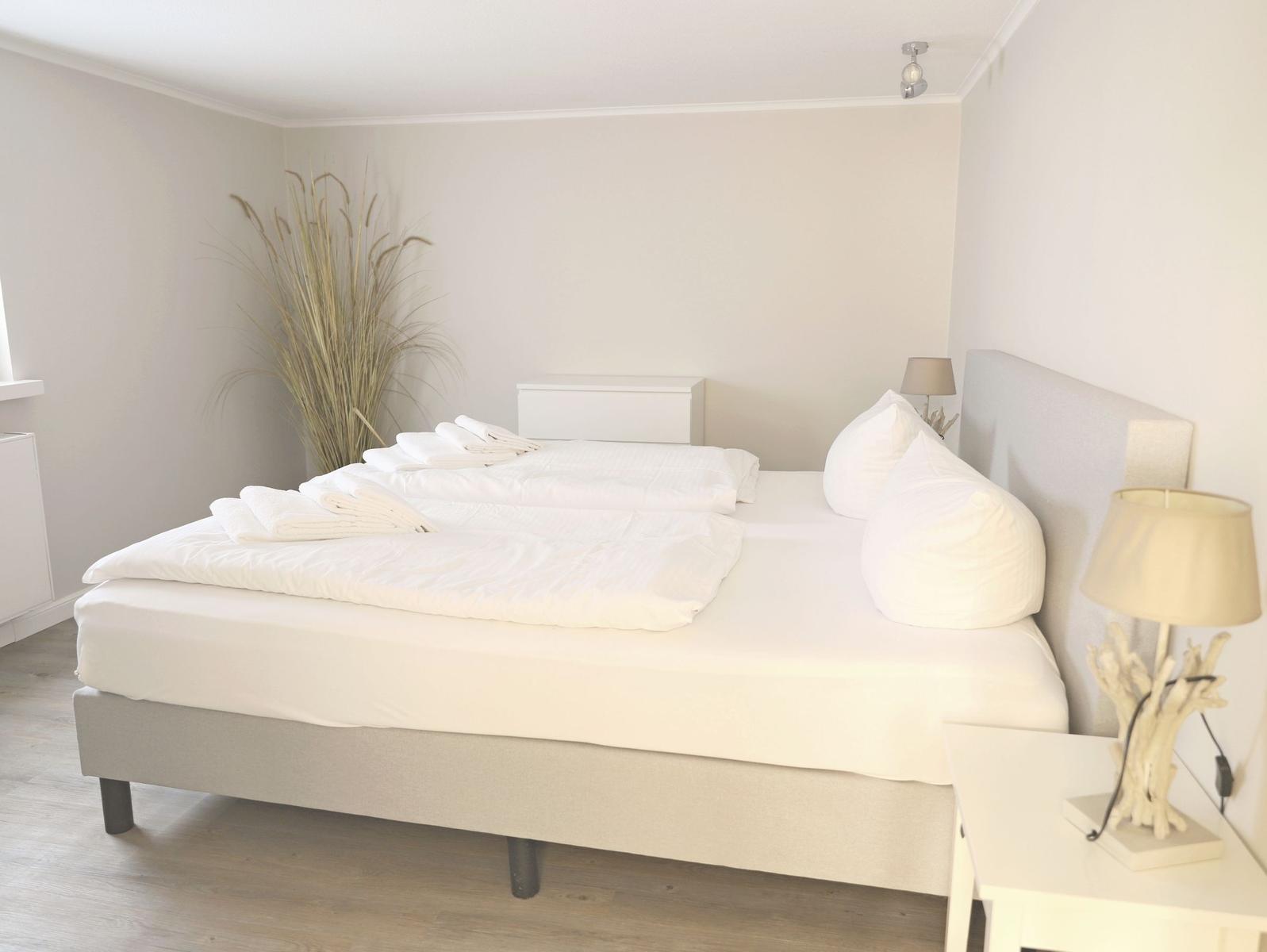 Schlafzimmer mit Doppelbett, Nachttisch und Pflanze.
