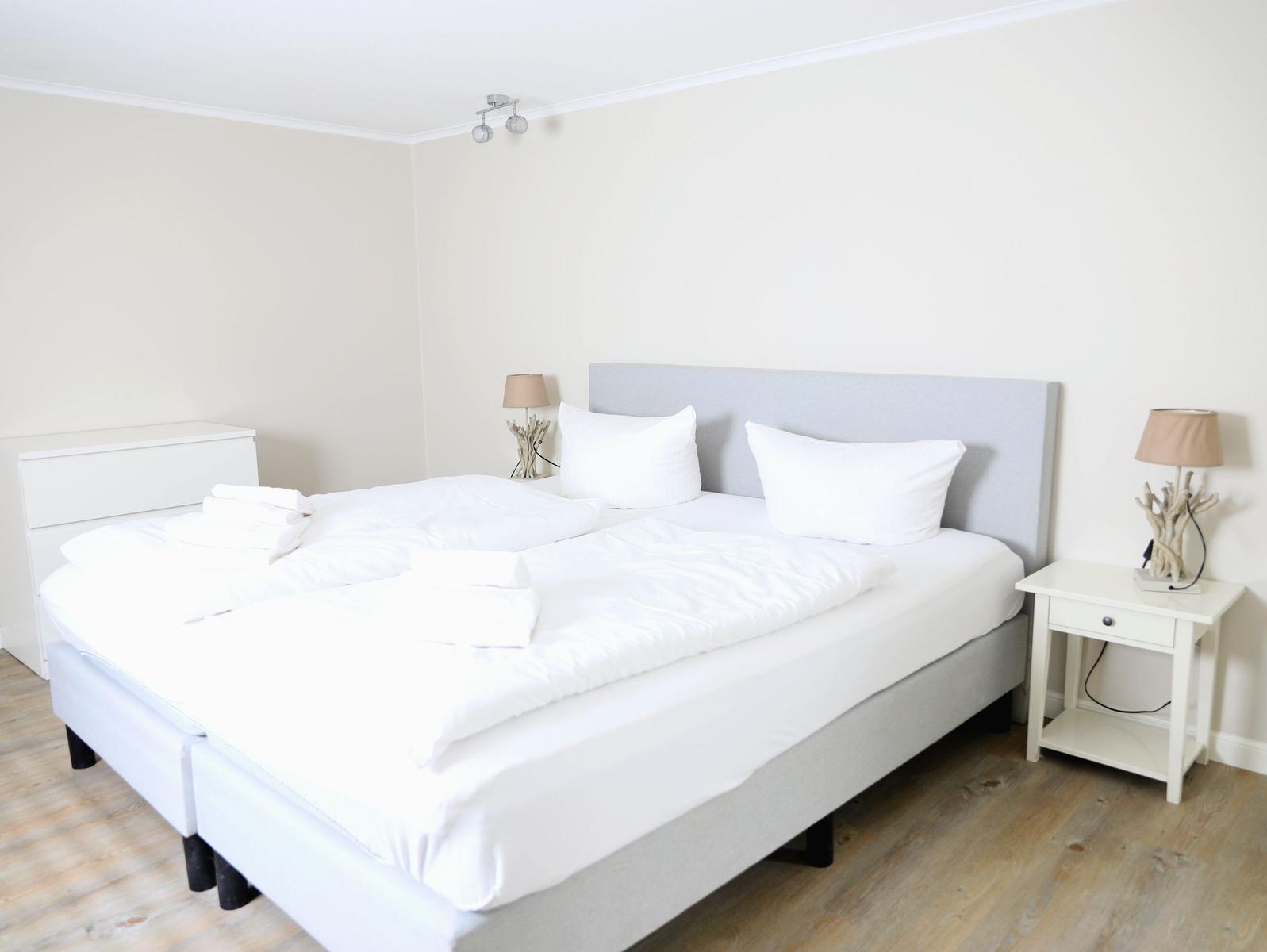 Schlafzimmer mit Doppelbett, Nachttischen und Lampen. Holzboden und weiße Wände.