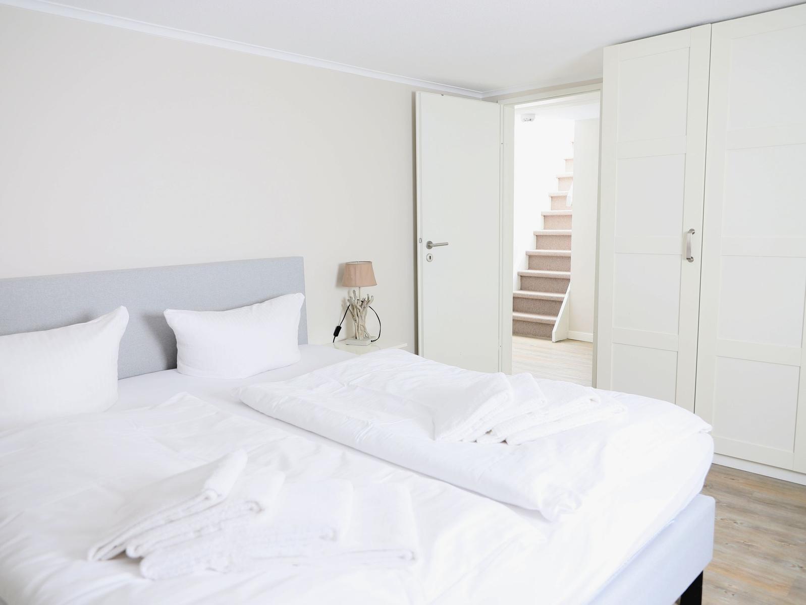 Schlafzimmer mit Doppelbett, Kleidung und Blick auf die Treppe.