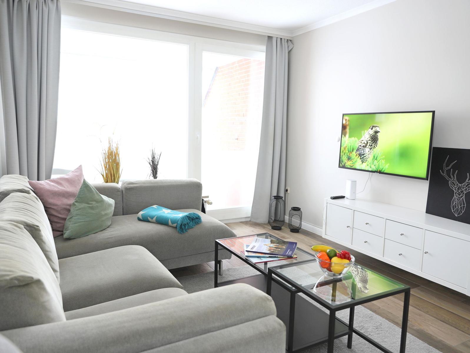 Wohnzimmer mit Sofa, Glas-Tisch und Fernseher an der Wand.