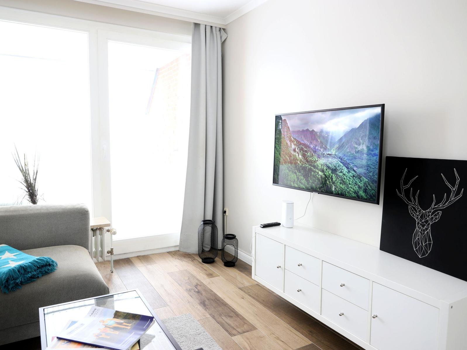 Ein Wohnzimmer mit grauem Sofa, Fernseher und Holzboden.