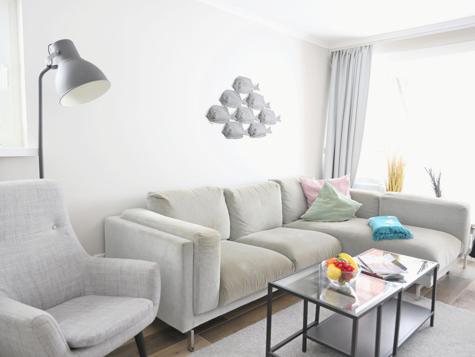 Ein Wohnzimmer mit grauem Sofa, Stehlampe und Glas-Tisch.