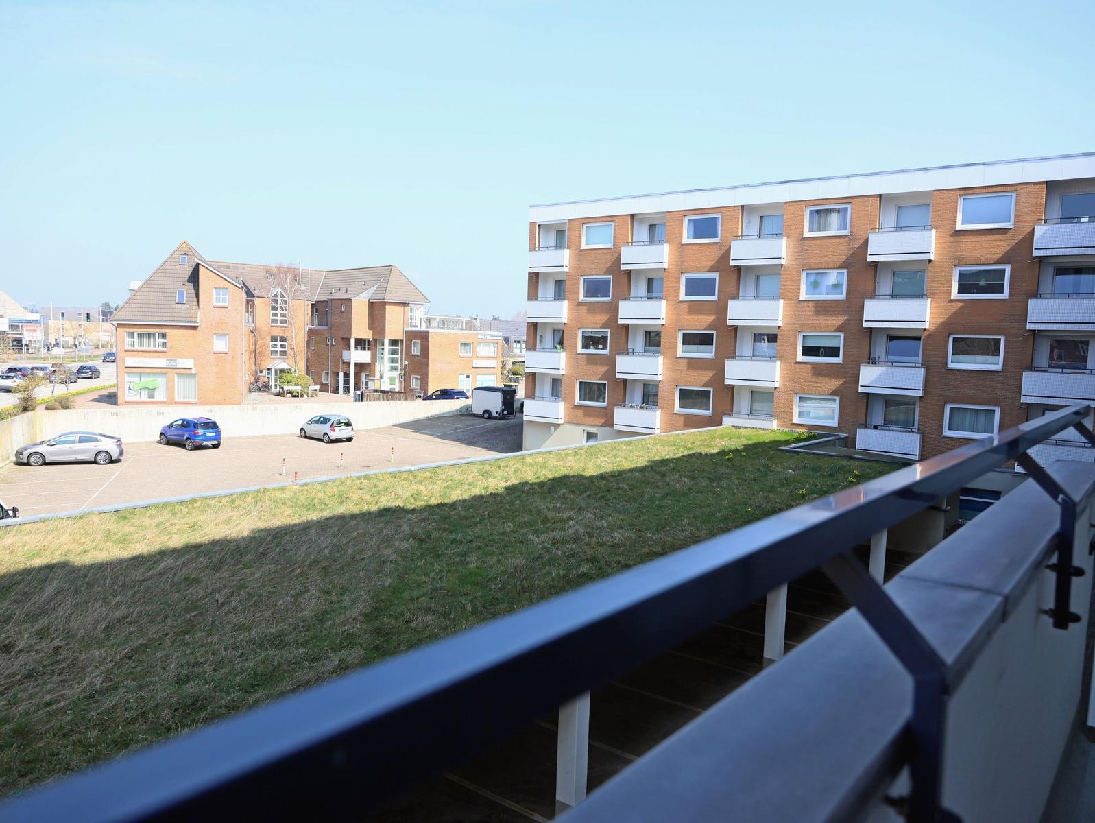 Blick von Balkon auf Wohngebäude und Parkplatz mit Autos.