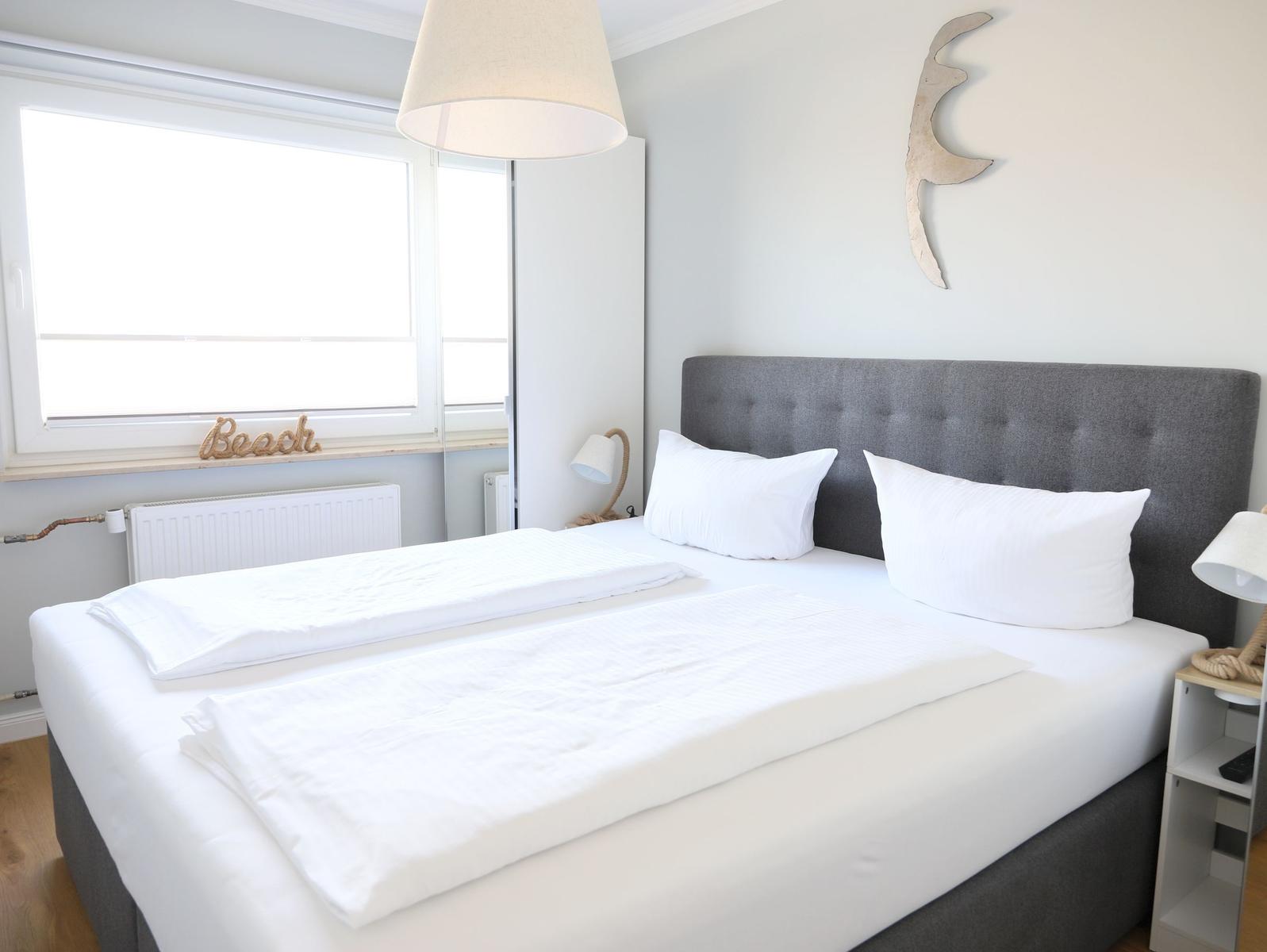 Schlafzimmer mit Doppelbett, Fenster und Wanddekoration.